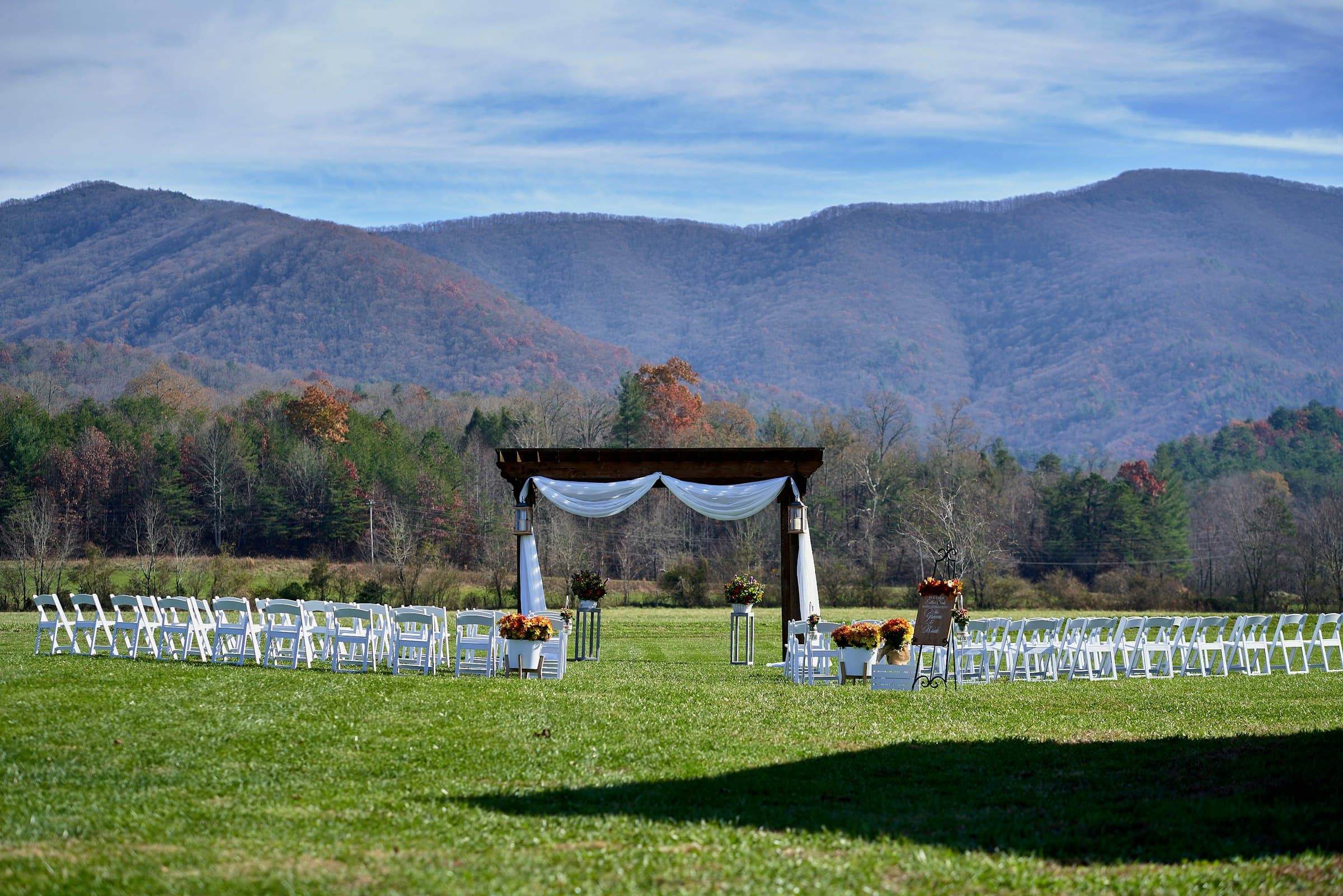 A wedding arch and white chairs in a green field below mountains