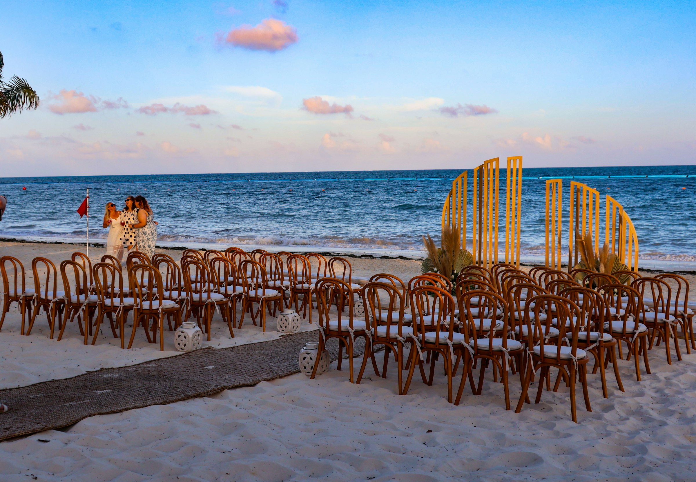 Wooden chairs arranged on the sand for a beach wedding at dusk