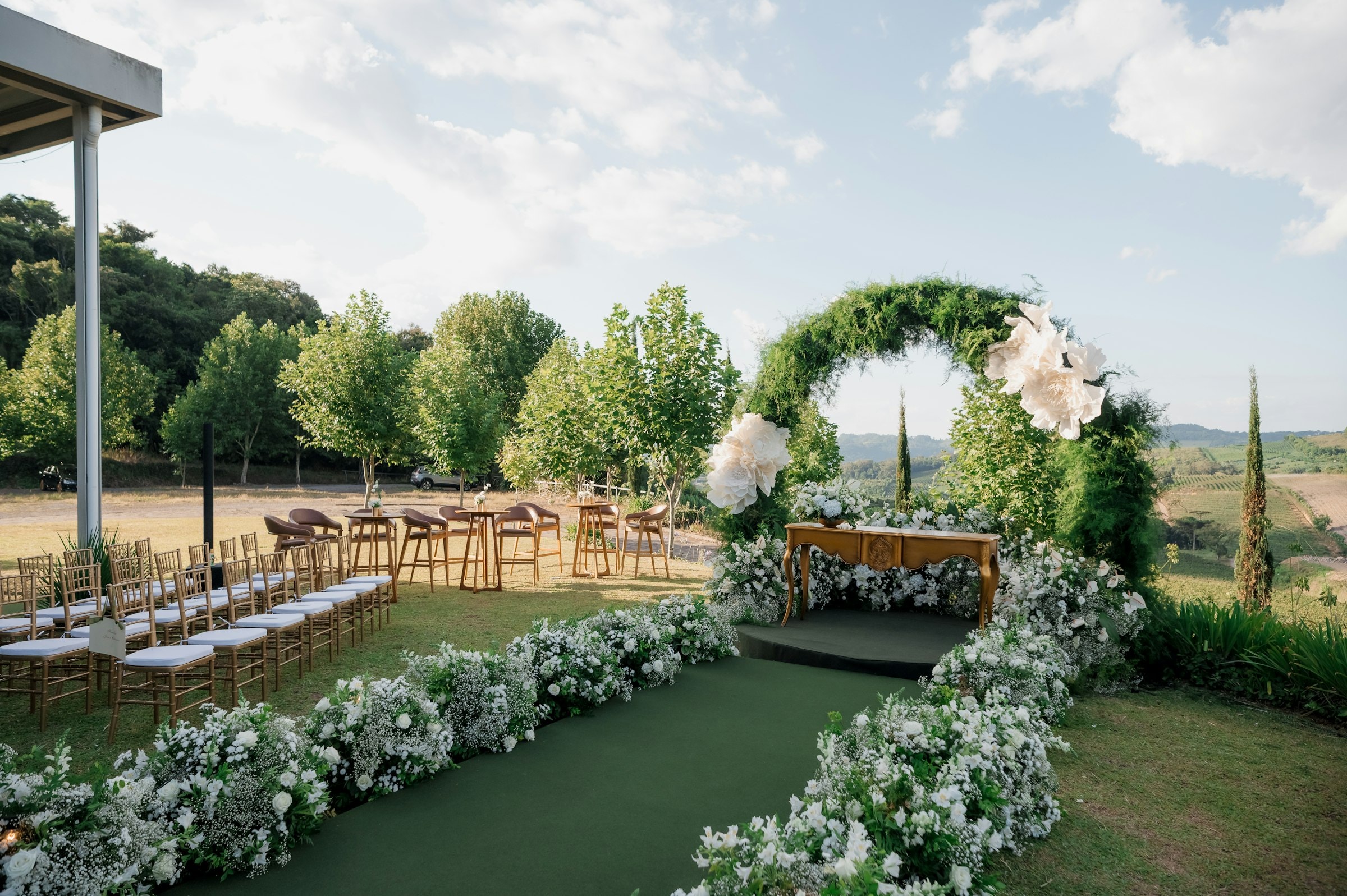 A garden wedding ceremony with a lush floral arch overlooking a green valley
