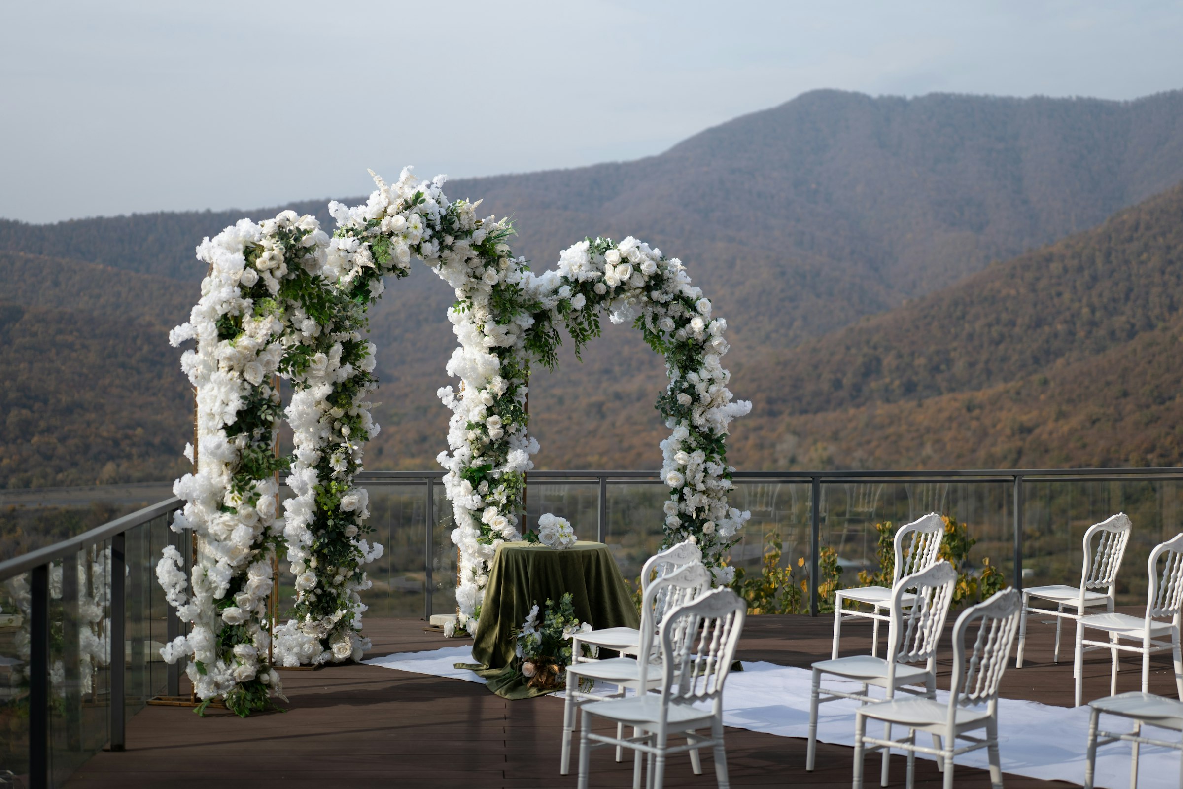 A wedding arch of white flowers on a terrace with mountains behind it
