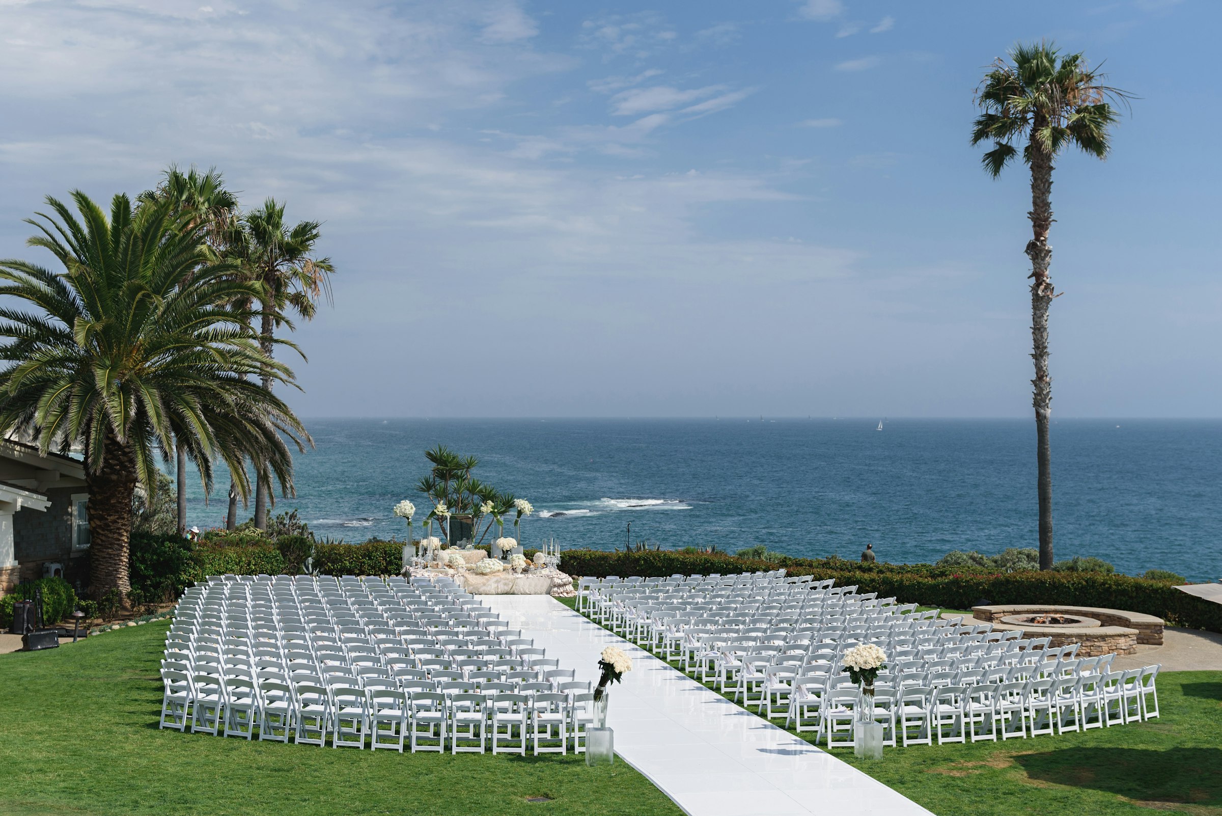 Rows of white chairs on a lawn overlooking the ocean, set for a wedding ceremony